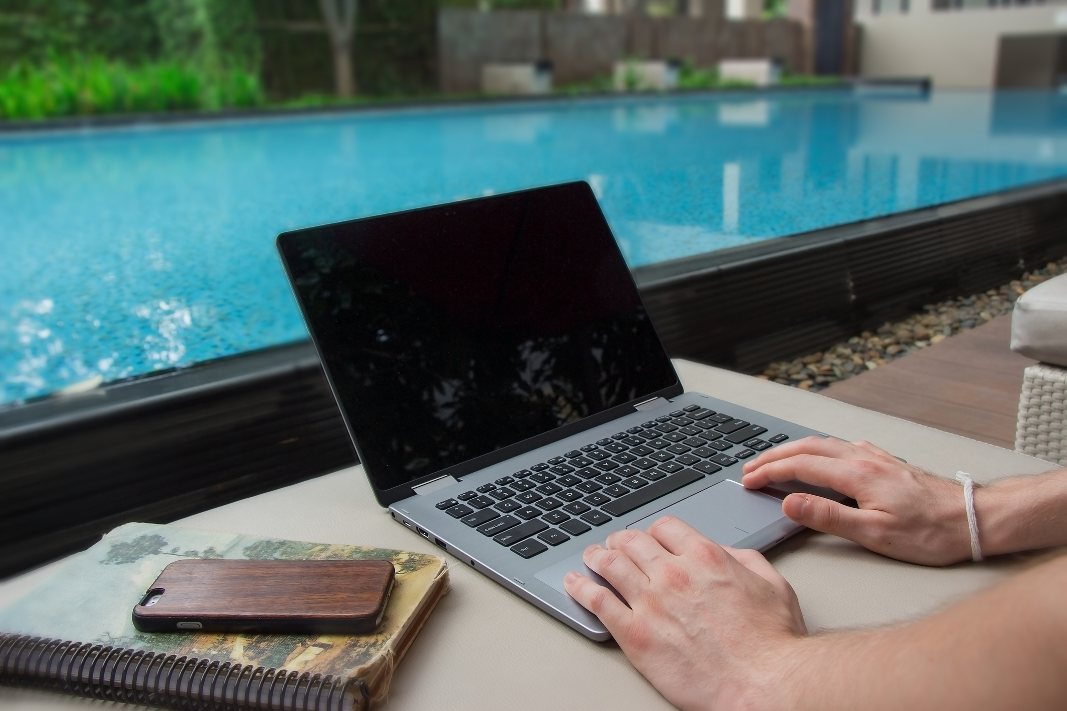 A person works from home on a laptop by a pool
