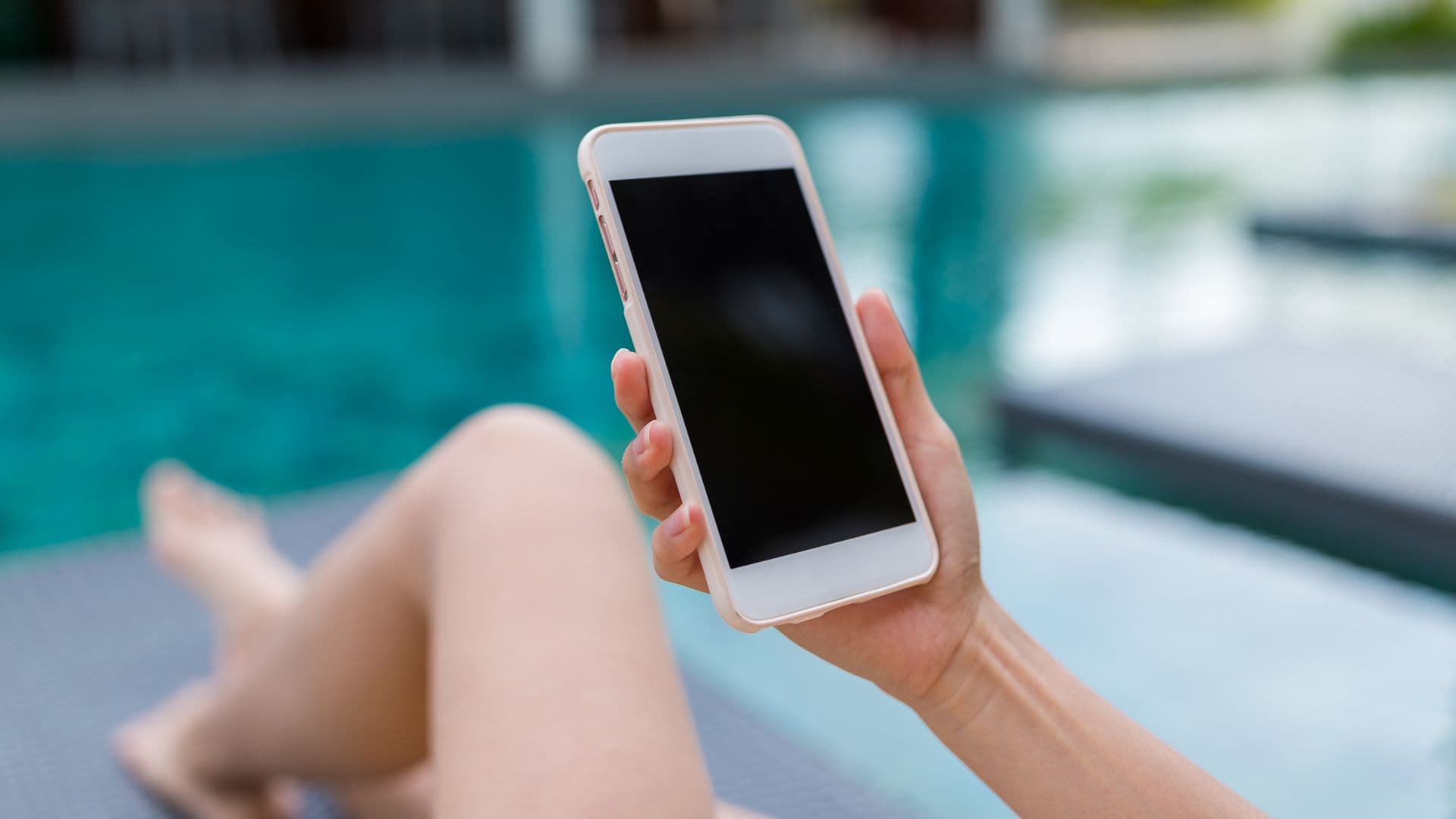 Woman looking at swimming pools ads on phone by swimming pool