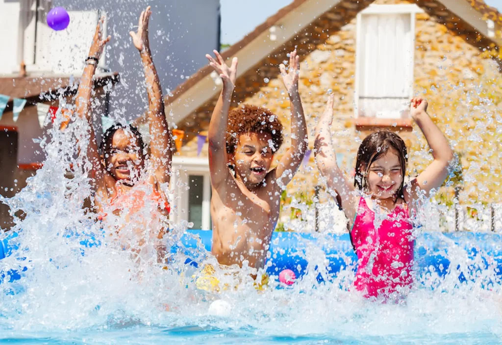 Three excited children splash in a pool.