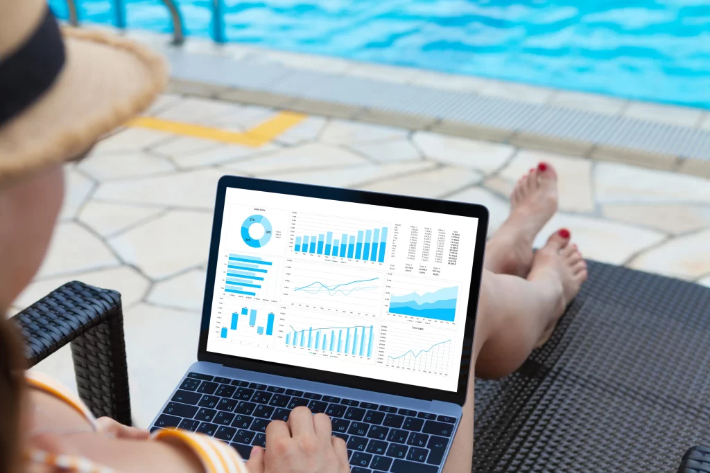 A person sitting in a lounge chair next to a pool looks at a laptop screen displaying pool and spa marketing metrics.